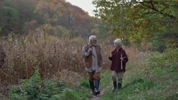 Abuelo con nieto caminando cerca del lago y llevando varillas — Vídeo de stock