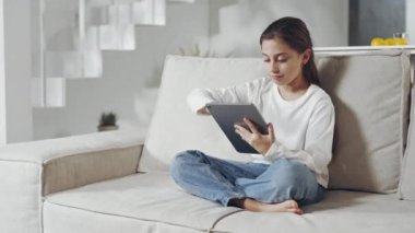 Liseli kız kanepede parmaklarını tablet ekranda kaydırıyor.