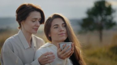 Büyüleyici kadınlar çay içip dışarıda konuşuyorlar.