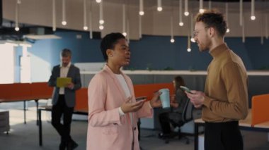İki çok ırklı çalışan ofis merkezinde duruyorlar, iş arasında gülümsüyorlar ve konuşuyorlar. İş adamları görüşlerini paylaşıyor toplantıda takım projesini tartışmaktan keyif alıyorlar.