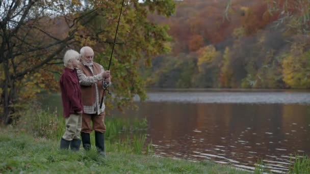 Homme âgé montrant petit-fils comment jeter la canne à pêche dans le lac — Video