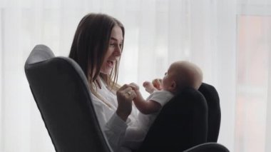 Çekici kadın sandalyede oturuyor ve yeni yürümeye başlayan bebekle oynuyor.