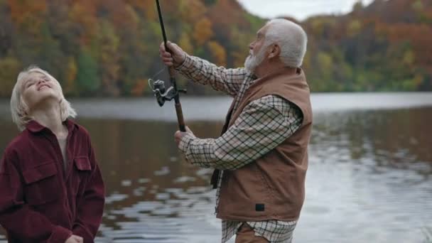 Abuelo ayudando a su nieto de fundición caña de pescar en el lago — Vídeos de Stock