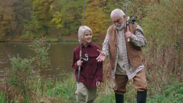 Grandfather and grandson with fishing rod walking near river — Stock Video
