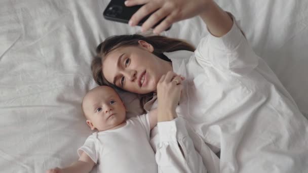 Счастливая мать лежит рядом с новорожденным ребенком и имеет видео чат — стоковое видео