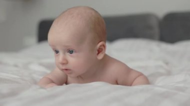 Mavi gözlü, beyaz yatakta sürünen tatlı bir erkek bebek.