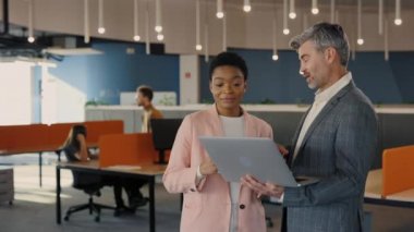 Yakışıklı bir ofis çalışanı dizüstü bilgisayardaki bayan iş arkadaşına bir şey gösteriyor. İş arkadaşları ellerinde kahve fincanlarıyla salonda durup ekrana bakıyorlar. İnsanlar ve teknoloji kavramı.