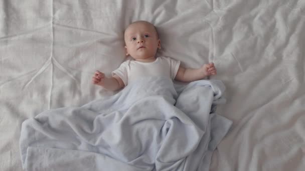 Милый мальчик лежит на кровати под мягким одеялом — стоковое видео