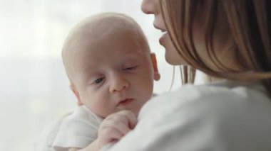 Genç bir kadın yeni doğmuş oğlunu kucaklıyor ve onunla konuşuyor.