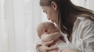Anne uykulu bebeğini öpüyor ve kucaklıyor.