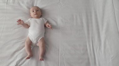 Sevimli yeni doğmuş bebek yatakta elleri ve bacaklarıyla hareket ediyor.