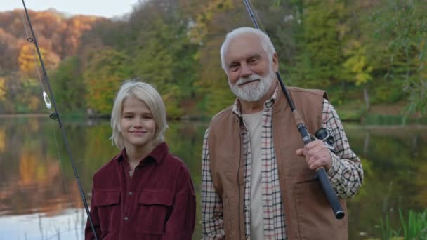 Avô com neto em pé perto do lago com varas de pesca — Vídeo de Stock