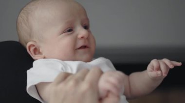 Yeni doğan çocuk annesinin ellerinde yatarken içtenlikle gülümsüyor.