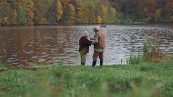 Abuelo y nieto de pesca con cañas en el lago — Vídeo de stock
