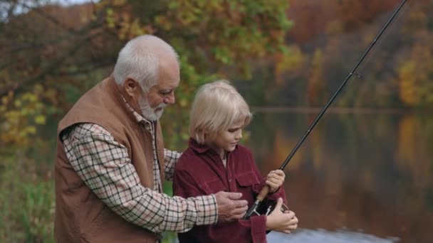 Ikääntynyt kalastaja selittää pojanpoikansa miten käyttää kehruu sauva — kuvapankkivideo