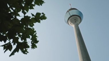 DÜKSELDORF, GERMANY - 1 Temmuz 2021: Rheinturm veya Rhine Kulesi, yüksek beton telekomünikasyon kulesi, mavi gökyüzü, park çevresindeki yeşil ağaçlar, Düsseldorf, Almanya.