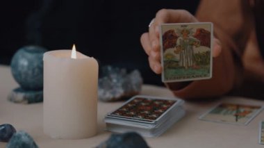 New York, ABD - 1 Mayıs 2021: Kameraya kart gösteren ve mum ışığında tarot kartları okuyan çingene falcıya yakından bakın. Kader kehanetleri ve kart konsepti üzerine büyülü bir oturum..