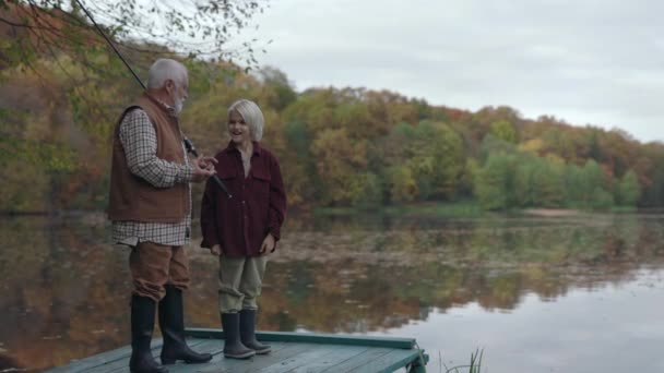 Tonårspojke och äldre man ler och småpratar på sjön piren — Stockvideo