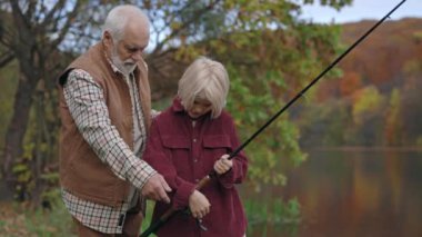 Senior man teaching his grandson how to use spinning rod