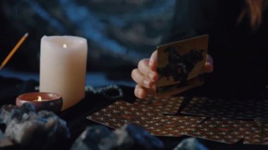 New York, USA - 1 May 2021: Female fortune teller showing Knight of Pentacles tarot card to the camera in the dark room. Magical pagan destiny reading ritual concept.