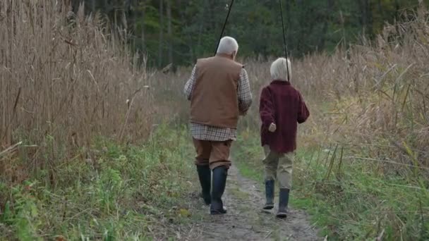Abuelo y nieto llevando cañas de pescar mientras caminan — Vídeo de stock