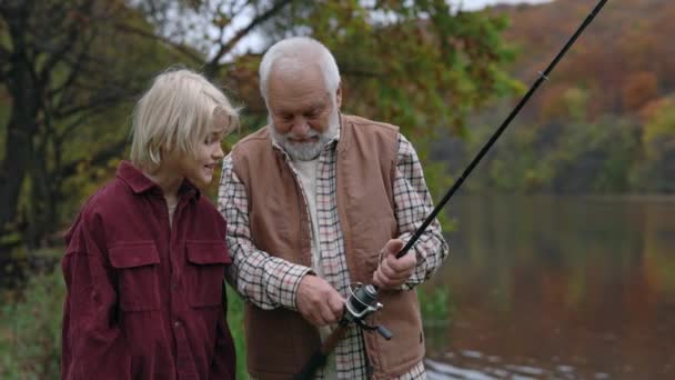 Aged fishman teaching his grandson fishing on lake — Vídeo de Stock