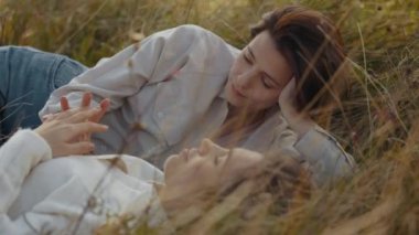 Güzel ve mutlu iki lezbiyen çimlerin üzerinde birlikte uzanırken birbirlerine nazikçe dokunuyorlar. Şefkat ve samimi duygular kavramı.