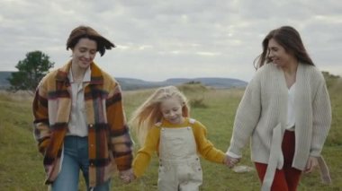 İki sevgi dolu kadın, dışarıda birlikte yürürken küçük tatlı kızlarıyla el ele tutuşuyorlar. Üç kişilik aile temiz havada konuşuyor ve gülümsüyor..