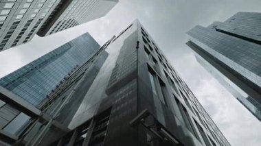 FRANKFURT, GERMANY - 2021 Ağustos: Modern gelecekçi gökdelenlerin cam cepheleri. Binaların alçak açılı görüntüsü yoğun trafiği olan bir set. Çerçevenin yavaş ve düzgün hareketi