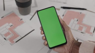 African american architects hand holding a phone on the background of the layout of their new apartment. Gadgets and content concept