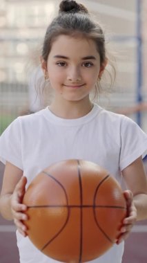Happy little caucasian girl standing on court holding ball and smilling. Sport concept
