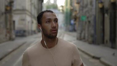 Erkek koşucu eski kasaba caddesinde koşuyor ve müzik dinliyor. Runner antrenman sırasında kulaklıkla müzik dinliyor. Yakın görüş. Spor ve sağlıklı yaşam tarzı kavramı