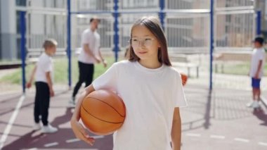 Elementary school girl standing at basketball court outside. Asian girl in glasses has a sport training with coach. Sport concept