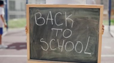 Hands of little boyst standing holding and raising schoolboard with text back to school on the street near school. Close up. Education concept