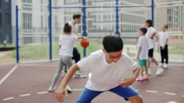 Asian boy in glasses trainings with ball on basketball court. schoolboy catching the ball and improve his skills in basketball