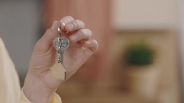 Close up of female hands holding key with house keychain in hand on the blurred background. New home and moving concept