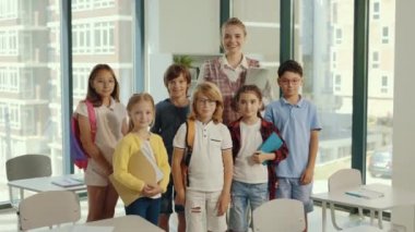 Portrait of elementary school pupils standing in classroom with female teacher in the middle of the class it the private school.People and educational concept