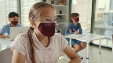 Side view of the asian girl sitting in a class listening the teacher wearing glasses and mask because of the pandemia. Education and health care concept