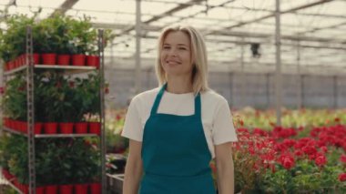 Portrait of the greenhouse gardener looking and smiling at the camera. Female worker florist crossing her arms standing on the greenhouse background. People and professions concept