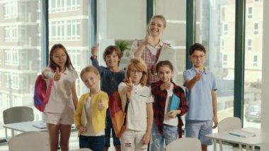 Portrait of the children stand with the teacher in the middle of the class and show a finger up feeling happy and cheerful together in the private school. People and educational concept