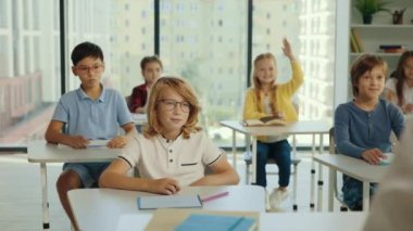 Elementary classroom of diverse bright children listening to the teacher giving a lesson. Everyone raises hand knowing the right answer. Brilliant kids in school learning science, creative thinking