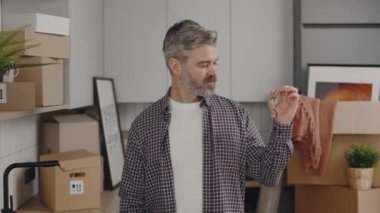Portrait proud happy man owner holding keys standing in own new apartment and boxes on the background. New home and moving concept