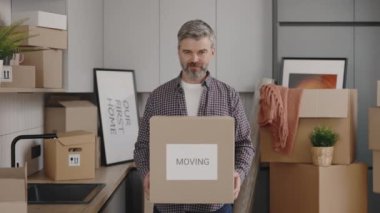 Portrait of middle aged man owner with boxes standing at new home. Cheerful husband caring paper boxe in slow motion. New home and moving concept