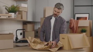 Sahibi eşyaları yeni evdeki kutuya koyar. Tabakları karton kutulara paketleyen yakışıklı adamın yeni daireye taşınması. Yeni ev ve taşınma konsepti