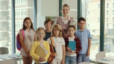 Öğretmen ve okul çocukları sınıfın ortasında birlikte duruyorlar. Sınıftaki bir grup ilkokul çocuğunun ve öğretmenin portresi. Halk ve eğitim kavramı