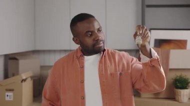 Kameraya göstererek, elinde anahtar tutan mutlu Afro-Amerikalı adama yaklaş. Gülümseyen erkek kiracı yeni daireye taşınmaktan memnun. Yeni ev ve taşınma konsepti