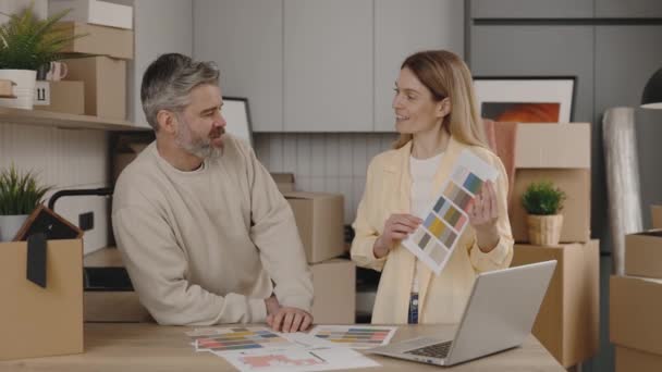 新しい家で壁を描くための色を選択する若い家族 夫と妻は家具のアパートを議論時計を保持 家の装飾と改装のコンセプト — ストック動画