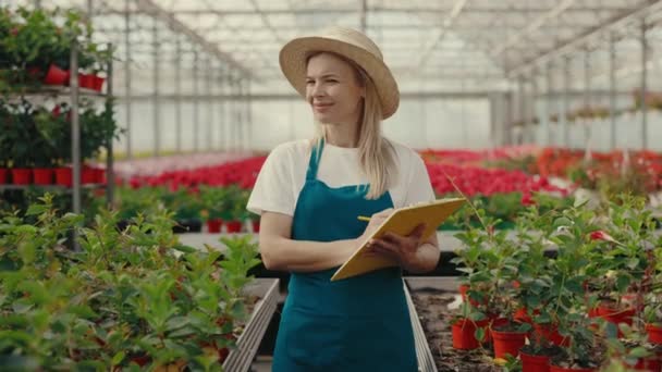 Female Gardener Wearing Hat Holding Tablet Standing Shelf Flowers Plants — Stock Video