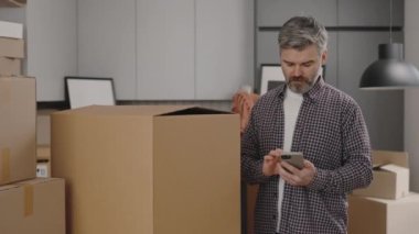 Orta yaşlı bir adam taşınırken telefon kullanıyor. Teslimat ve taşınma konsepti