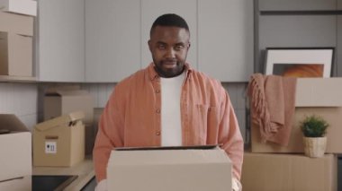 Kameraya gösterilen, elinde büyük bir kutuyla mutlu bir Afrikalı Amerikalı 'nın portresi. Gülümseyen erkek kiracı yeni daireye taşınmaktan memnun. Gayrimenkul. Yeni ev ve taşınma konsepti